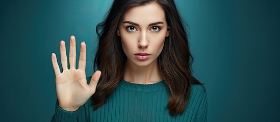 The woman is creating a stop sign with her hand, using her fingers and thumb to form the gesture. Her hand stands out against her electric blue shirt