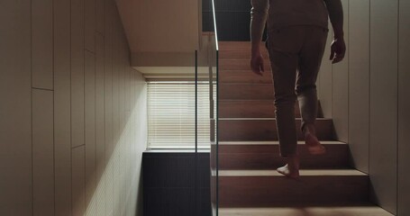 Cropped view on barefoot man go upstair on second floor of modern house. Male go up on staircase at contemporary apartment