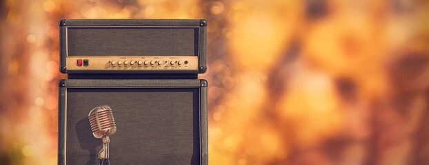 Big guitar amplifier speaker cabinet and control head with vintage microphone in front of a colorful background with copy space