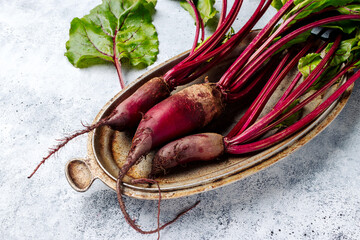 Fresh raw beets with leaves on a rustic metal dish on a gray background