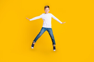 Fototapeta na wymiar Full length photo of carefree positive kid dressed white shirt arms sides jumping high empty space isolated yellow color background