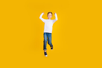 Full length photo of cheerful lucky kid dressed white shirt rising fists jumping high empty space...