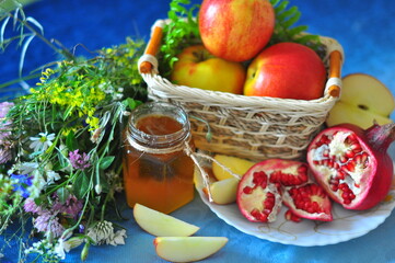 Apples in a wicker basket, pomegranates, honey in a glass jar and wildflowers