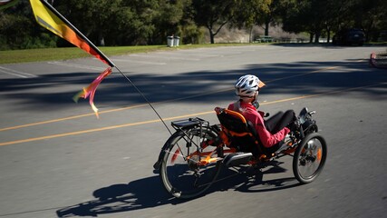 Elderly senior woman riding recumbent tricycle e-bike on a path on a sunny day in a park.
