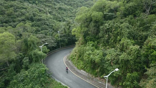 drone shot of a young asian female cyclist riding bike on rural asphalt road