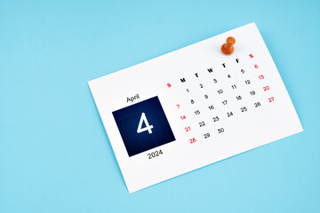 Fototapeta na wymiar April 2024 calendar page with push pin on blue background.