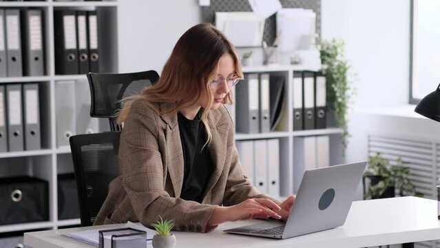 Portrait of a successful and smiling young Caucasian businesswoman or accountant working with laptop in office. Female boss or chief looking at camera.