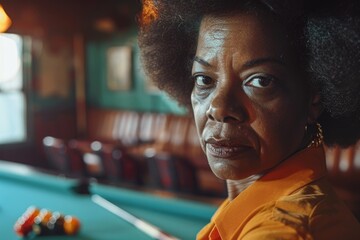 A woman in an orange shirt sitting in front of a pool table. Ideal for leisure and recreation concepts - obrazy, fototapety, plakaty
