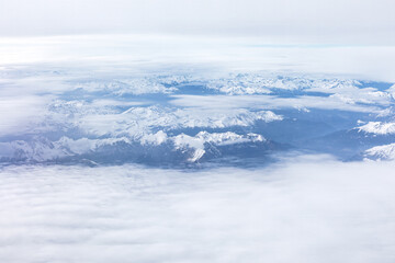 Fototapeta na wymiar Snow covered mountains view through the clouds from above