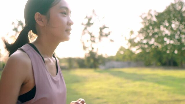 A beautiful Asian woman is jogging in a park in the amber-orange evening sun, A woman with long dark hair jigs and wants to stay in shape, Exercise to stay healthy.