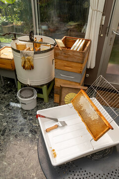 Apiculture - A la miellerie - Cadre de r&eacute;colte rempli de miel pos&eacute; dans sur un bac &agrave; d&eacute;soperculer devant un extracteur et des hausses