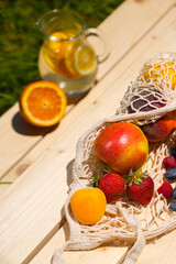 Lemonade and fresh fruits at a picnic. Close up healthy eco bio fruits food on a wooden table in the middle of summer. Oranges, lemons, apples, peaches and strawberries. 