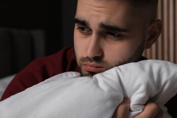 Sad young man with pillow at home