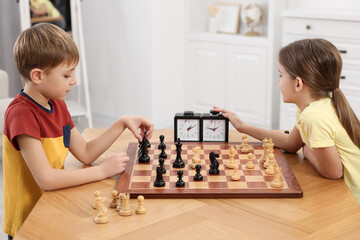 Cute children playing chess at table in room
