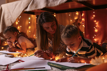 Obraz na płótnie Canvas Mother and her children drawing in play tent at home