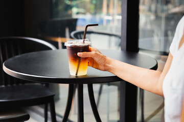 Woman drinking iced coffee in takeaway plastic cup at table outdoor cafe.