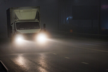 A vehicle with automotive lighting is rolling down the foggy highway at midnight. The headlamps...