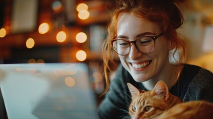 with glasses smiles while working at a laptop with a cat at the workplace