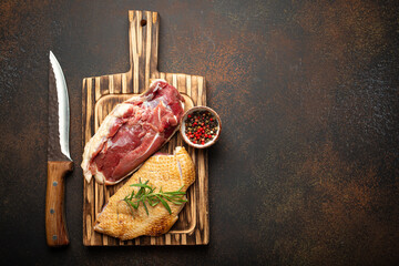 Two raw uncooked duck breast fillets with skin, seasoned with salt, pepper, rosemary top view on wooden cutting board with knife, dark brown concrete rustic background, space for text. - 761506053