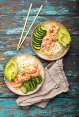 Two white ceramic bowls with rice, shrimps, avocado, vegetables and sesame seeds and chopsticks on colourful rustic wooden background top view. Healthy asian style poke bowl. - 761506247