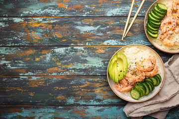 Two white ceramic bowls with rice, shrimps, avocado, vegetables and sesame seeds and chopsticks on...