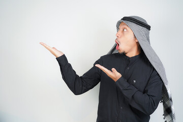 Wow face shocked expression Asian Muslim man wearing Arab turban sorban pointing hand finger at empty space