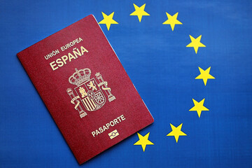 Red Spanish passport of European Union on blue flag background close up. Tourism and citizenship...