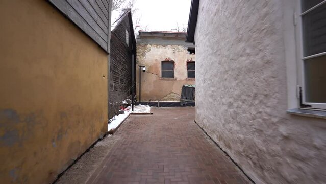  shows a narrow alley with brick pavement between an old yellow building and a white modern building with metal gate