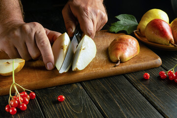 Chef hands cut a pear with a knife on a cutting board to prepare compote or fruit juice. The...
