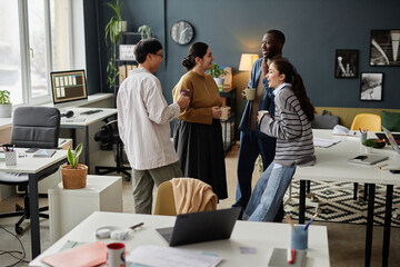 Diverse group of four cheerful colleagues in animated communication during coffee break in office - obrazy, fototapety, plakaty