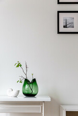 Tree branch or plant growing in a glass green vase. Hygge concept. Seashell ceramic vase and candle flower. Spring stylish decoration. Easter. Mimimalism. White wall background. Eco home.