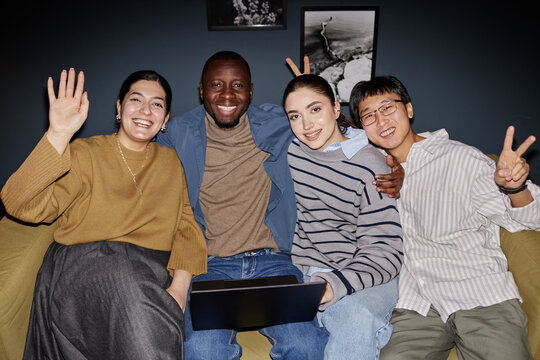 Portrait of carefree multiethnic business team waving at camera while posing together in office, shot with flash