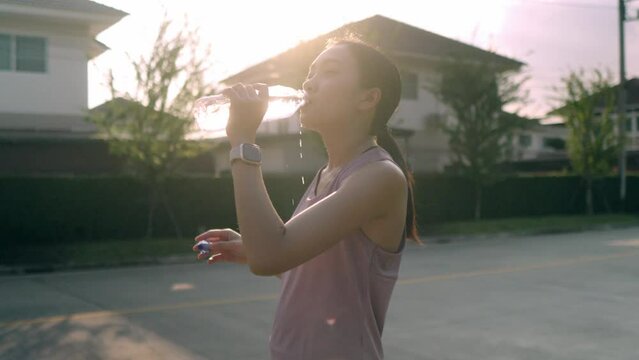 A young Asian woman who had just finished a running workout was resting while drinking electrolyte water to quench her thirst and sweat, Drink water to relieve fatigue after exercising for a while.