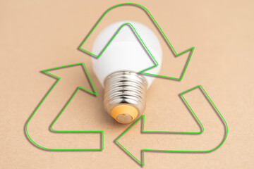 A light bulb is on a table next to a green recycling symbol.