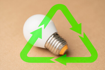 A light bulb is on a table next to a green recycling symbol.
