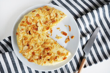 Almond cake on a white plate on a striped towel next to a fork and knife  on a light background