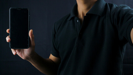 Asian man holding big smartphone with blank screen in hand, showing close to camera and pointing at device. Gadget with empty free space for mock up, banner