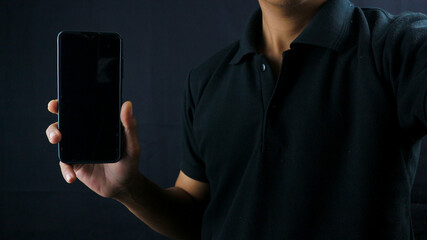 Asian man holding big smartphone with blank screen in hand, showing close to camera and pointing at...