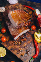 roasted pork ribs in a smokehouse, standing on a cutting board, garnished with rosemary, pepper, chili pepper, tomato, lemon, pomegranate. aromatic baked meat
