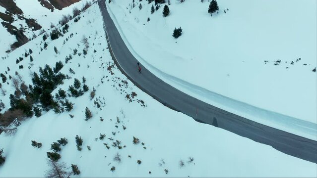 Two cyclists pass in front of camera on descend from mountain top on professional carbon road bikes. Ride fast on the way to finish line in extreme cold winter conditions