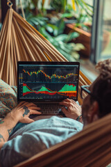 Successful rich stock trading investor, man trader or broker relaxing in hammock on nature using laptop computer investing money in rising financial market analyzing charts on screen. Over shoulder.