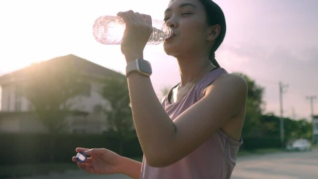 A young Asian woman who had just finished a running workout was resting while drinking electrolyte water to quench her thirst and sweat, Drink water to relieve fatigue after exercising for a while.