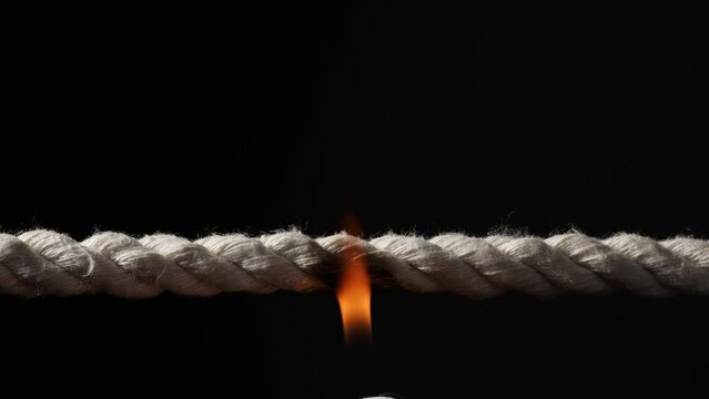Rope stretched tight and slowly burning apart, finally snapping in two. Concept of dangerous stress or stressful situation like divorce separation, deadlines, failure, or tension.