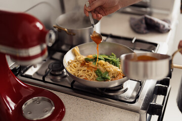 Pouring sauce over pasta in a pan, home cooking concept, kitchen setting - Powered by Adobe