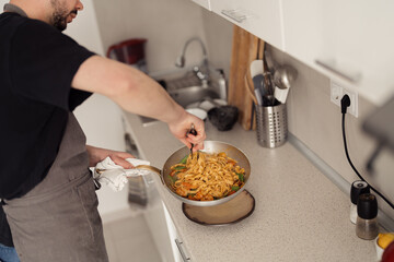 Man cooking pasta in a modern kitchen, focus on stir-frying in pan