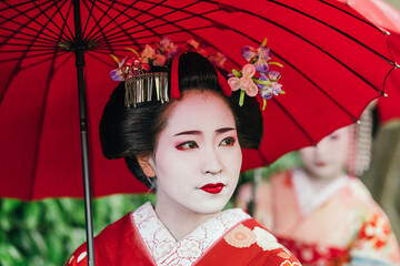 A geisha's reflective gaze under a red umbrella captures the depth of Japanese cultural heritage. Her red kimono is a visual symphony of tradition and craftsmanship