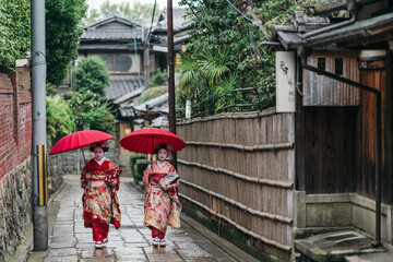 Geishas navigate the wet cobblestones of Kyoto in their radiant attire, the red umbrellas a poetic touch to the grey skies. They move with a grace that honors their cultural legacy