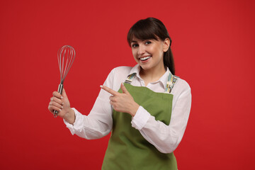 Happy professional confectioner in apron pointing at whisk on red background