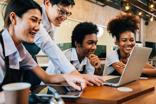 Owner and young business team in coffee shop collaborate on project using laptop. Startup teamwork concept colleagues brainstorming planning together for success.