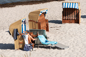 Strandsituation im Sommer zwei Beinenpaare schauen aus dem Strandkorb auf einem Sandstrand - 761557629